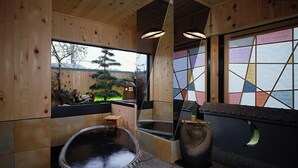 Un onsen japonés tradicional con interior de madera, un manantial termal de piedra y vistas del paisaje circundante.