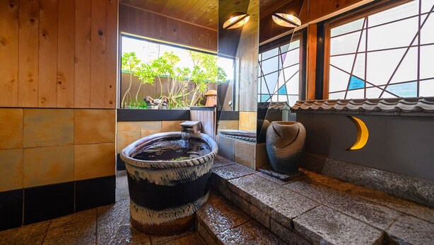 Un baño de estilo japonés tradicional con un lavabo de piedra, una pared de madera y vistas a la vegetación exterior.