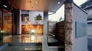 Entrada de hotel con un muro de piedra, una puerta de cristal y un pequeño árbol.