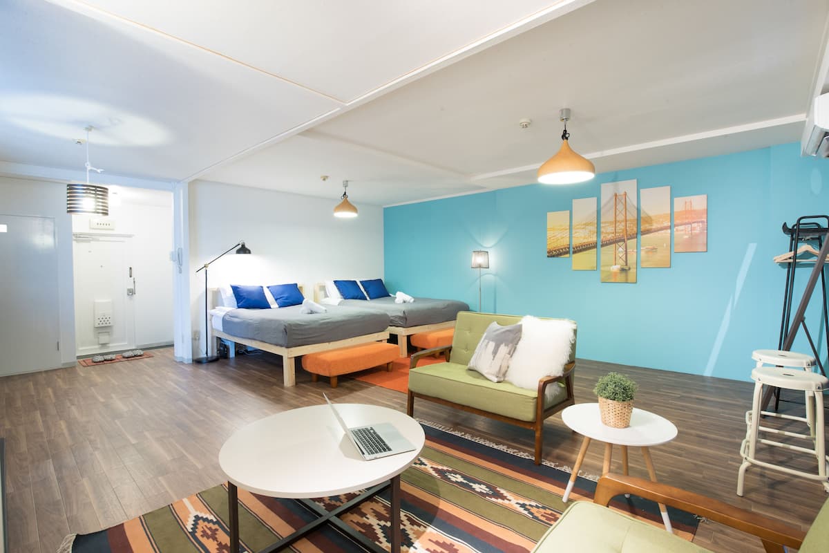 Una habitación moderna con una cama, un sofá verde, una pequeña mesa con una computadora portátil y una silla blanca.