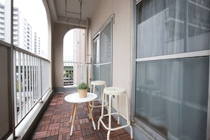 A balcony with a brick floor, two white stools, a small round table, and a potted plant.