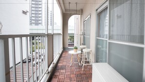 A balcony with a tiled floor, a small round table with a potted plant, and two white chairs. - Namba Hara Apartment (Osaka)