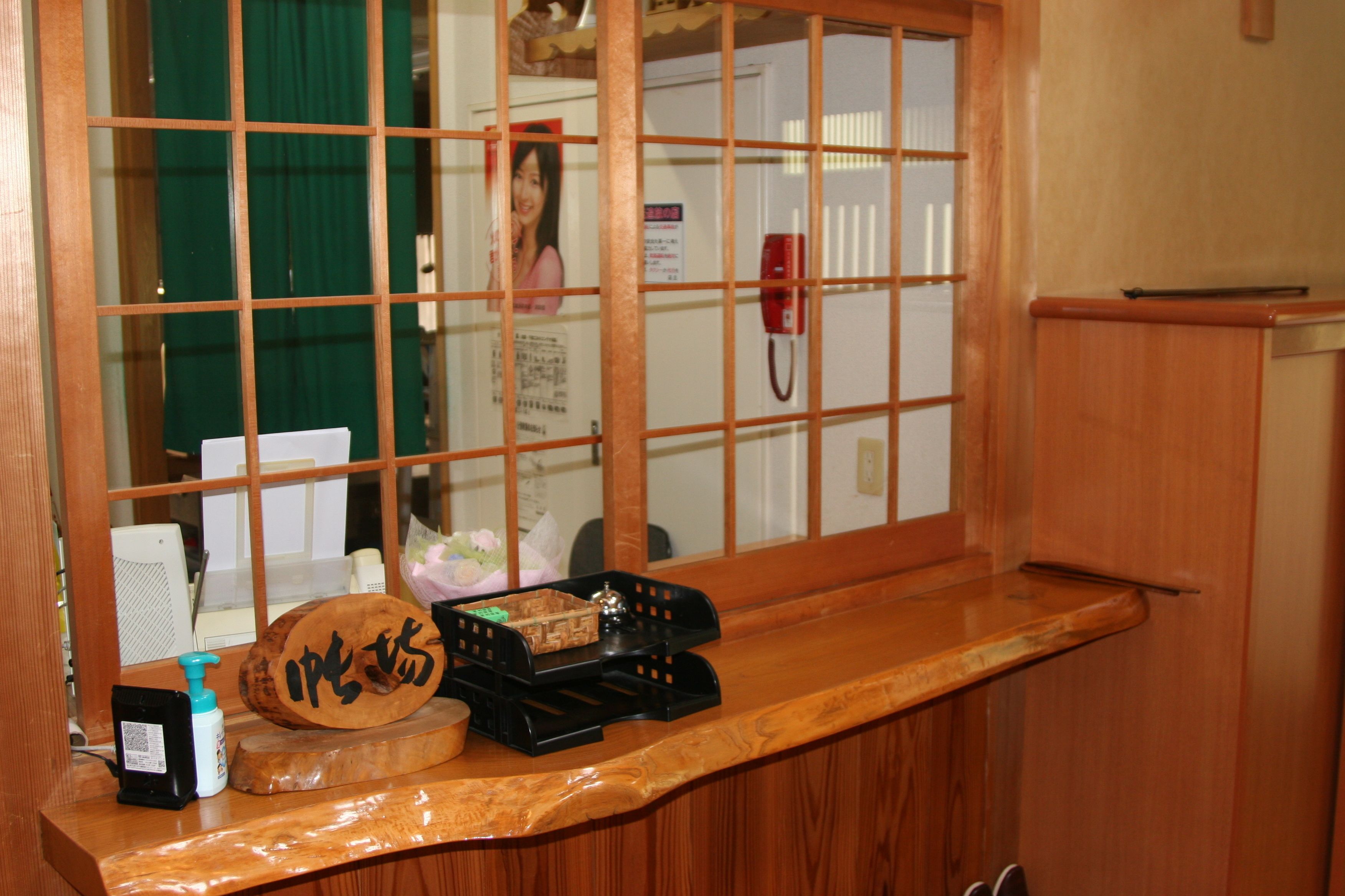 A wooden counter with a wooden plaque, a black telephone, a small black box, and a bottle of hand sanitizer.
