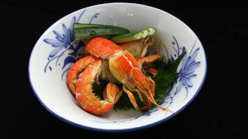 A bowl with a floral pattern containing a crab, cucumber slices, and green leaves.
