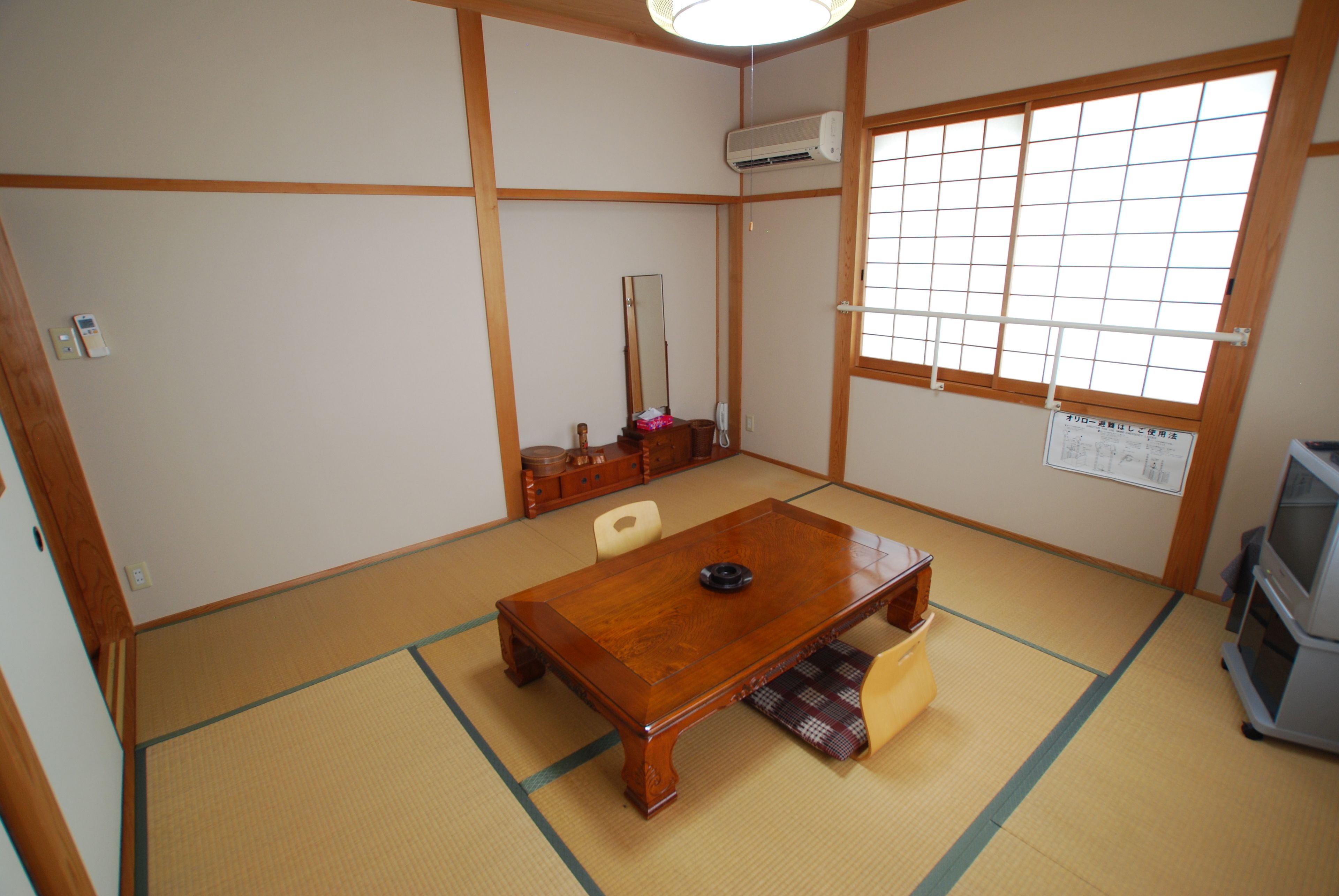 A traditional Japanese room with tatami flooring, a wooden table, a television, and a shoji screen.