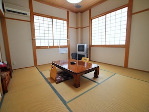 A tatami mat room with a wooden table, chairs, a television, and a radiator. - Shokinkan (Uki)