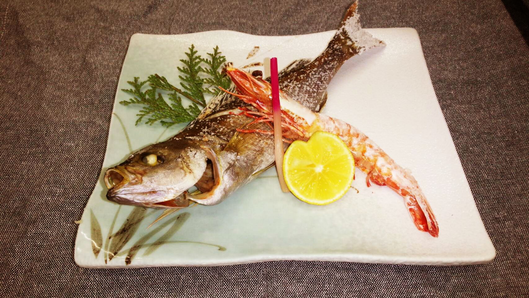 A fish dish on a white plate with a lemon slice and garnish.