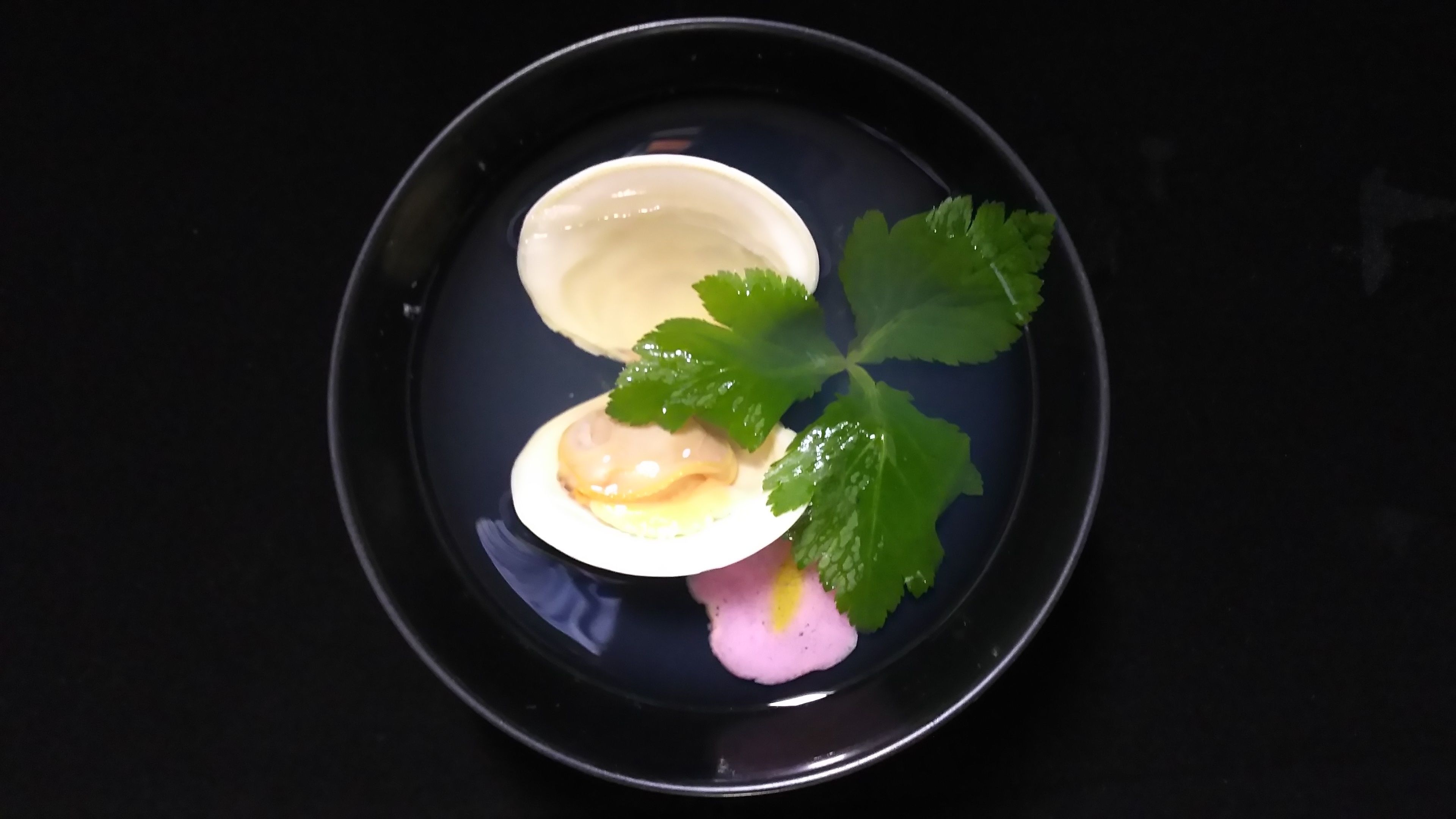 A plate with a white bowl containing a pink substance, a green leaf, and a small white object.
