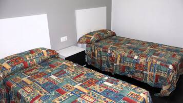 Una habitación con dos camas individuales, cada una con un colcha colorida, una mesita de noche blanca y una pared gris.