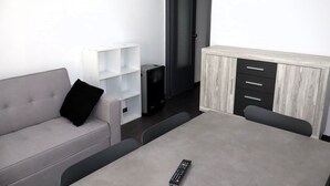 A modern living room with a grey sofa, a white shelving unit, a grey dining table, and a black speaker. - Los Monegros (Peñiscola)