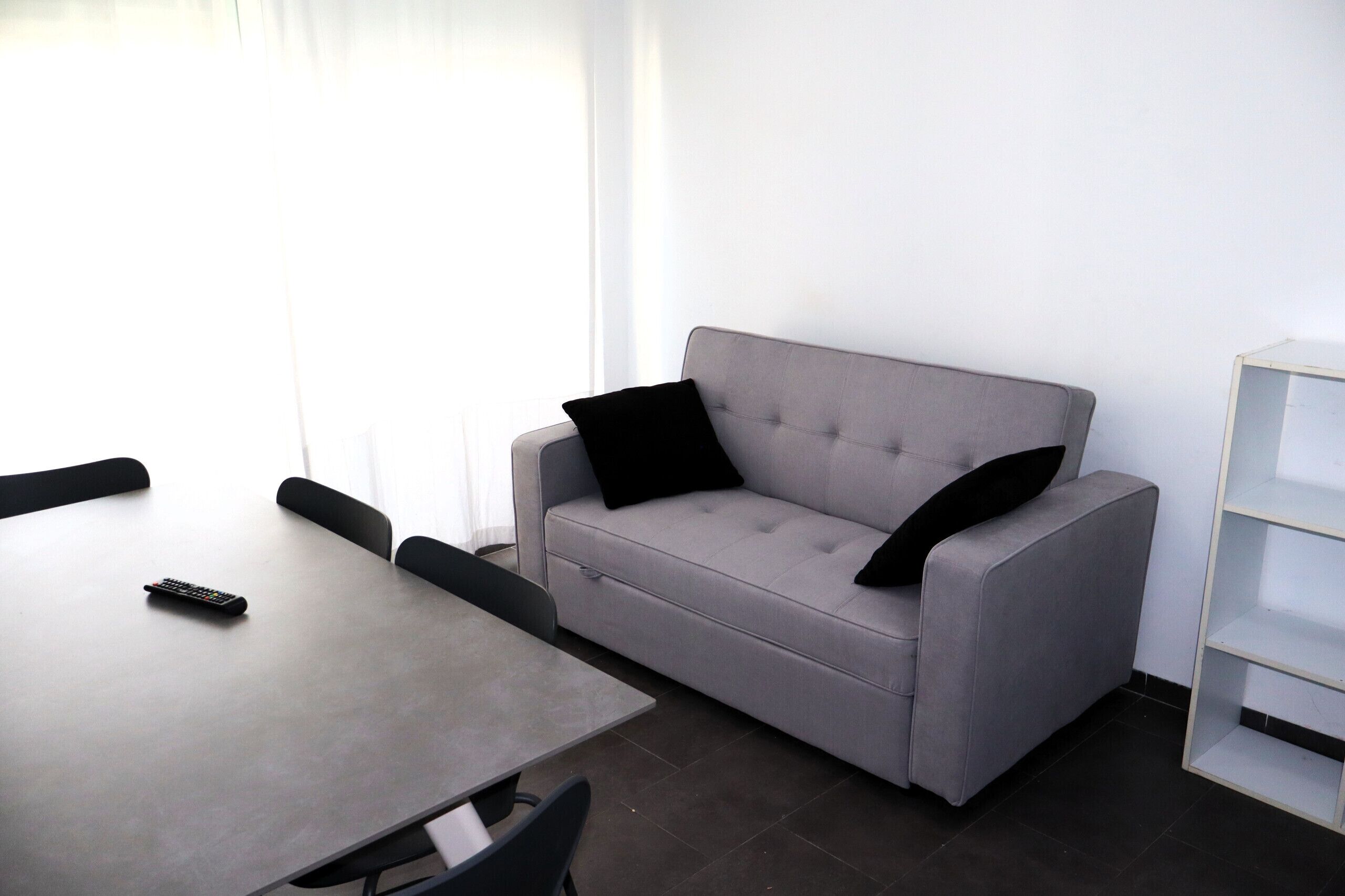 Une pièce moderne avec un canapé gris, une petite table et une étagère blanche.