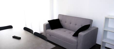 Une pièce moderne avec un canapé gris, une petite table et une étagère blanche.