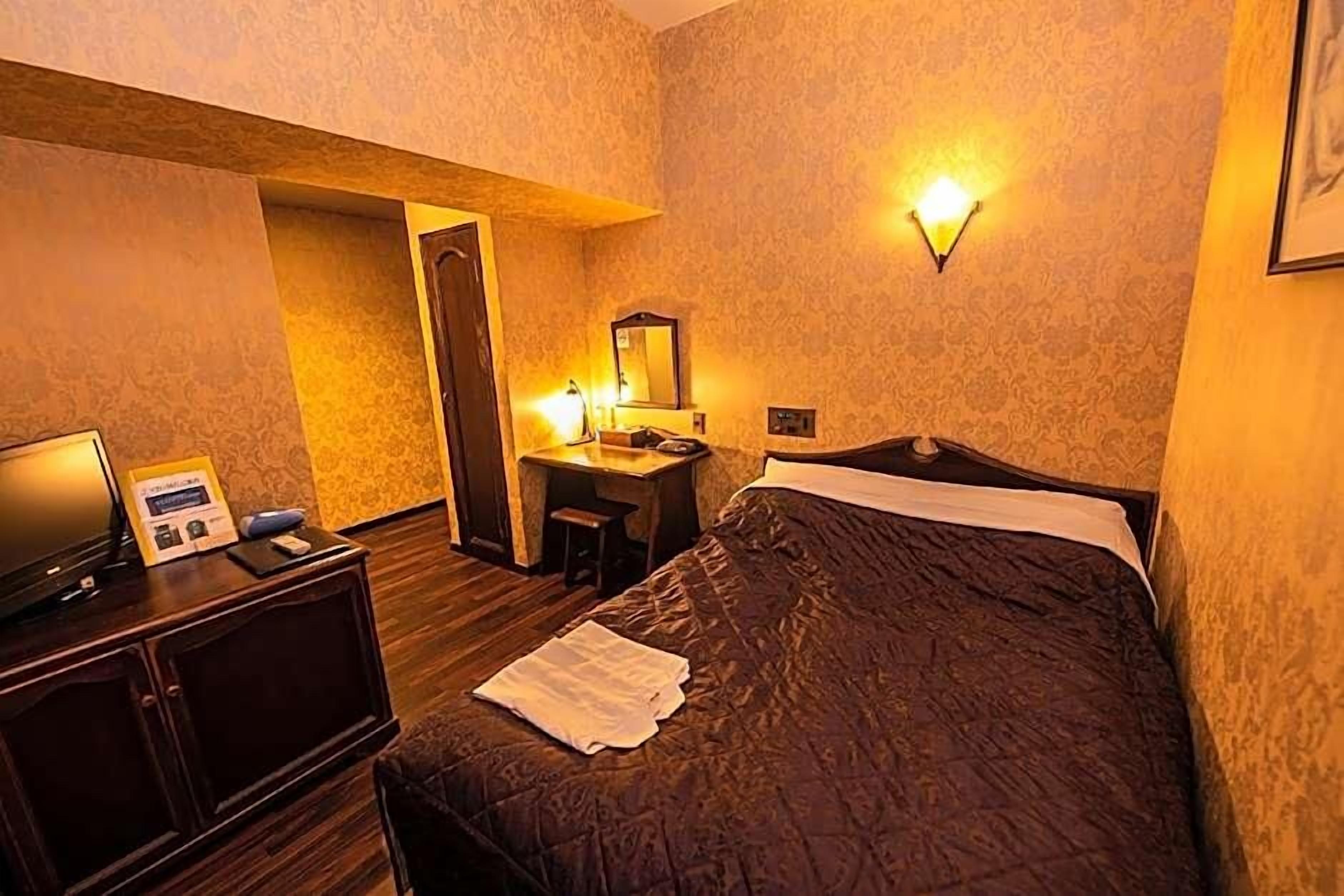 A hotel room with a bed, a desk with a mirror, and a wall-mounted light fixture.