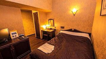 A hotel room with a bed, a desk with a mirror, and a wall-mounted light fixture.