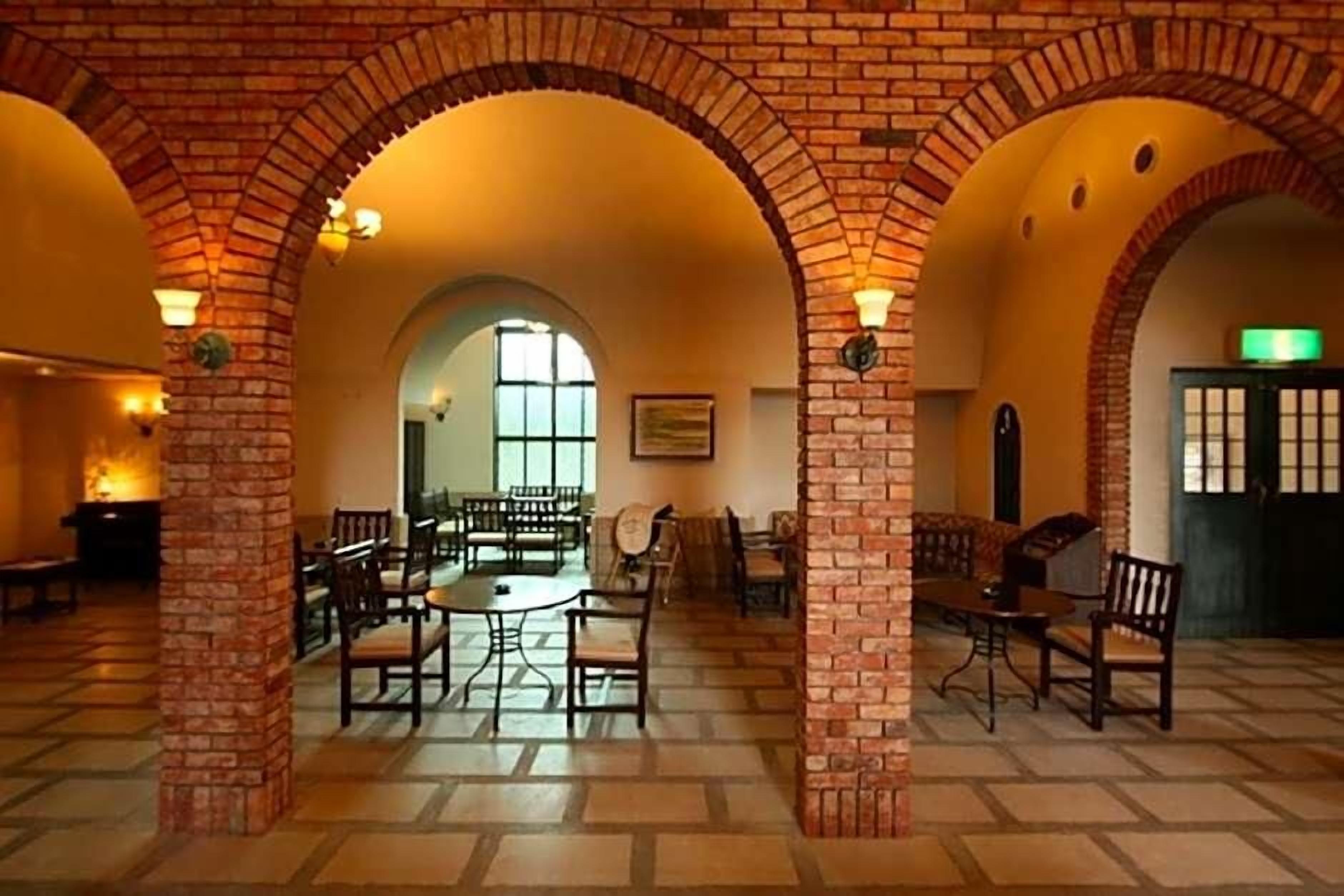 A spacious interior with brick arches, a central dining area with tables and chairs, and a view through an arched doorway.
