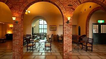 A spacious interior with brick arches, a central dining area with tables and chairs, and a view through an arched doorway.