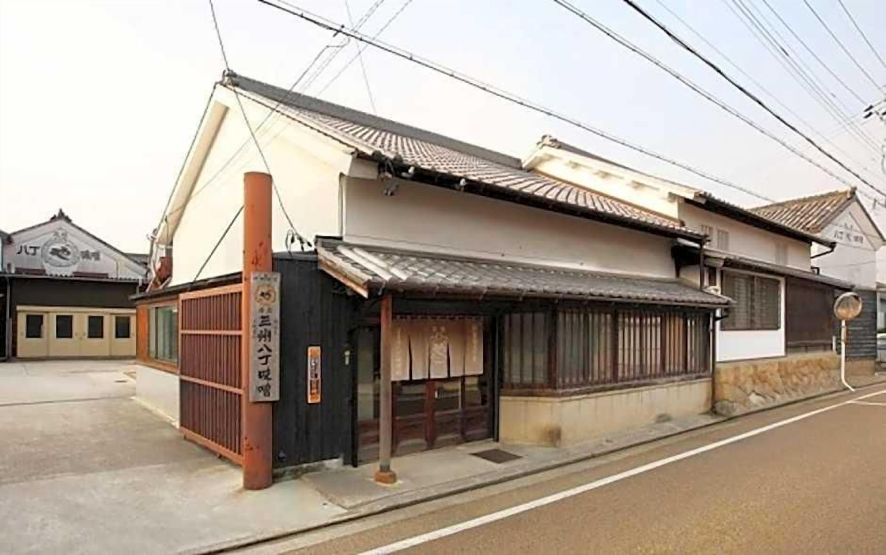 A traditional Japanese building with a tiled roof, a wooden entrance gate, and a signboard.
