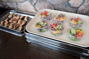 Un plateau contenant divers aliments, notamment ce qui semble être du poisson grillé et une variété de salades de légumes et de fruits.