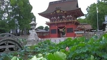Um edifício japonês tradicional com telhado curvo, cercado por vegetação exuberante e uma ponte de pedra.