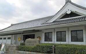 Ein traditionelles japanisches Gebäude mit einem Ziegeldach, einem steinbelagten Weg zum Eingang und einem Schild mit japanischen Schriftzeichen.