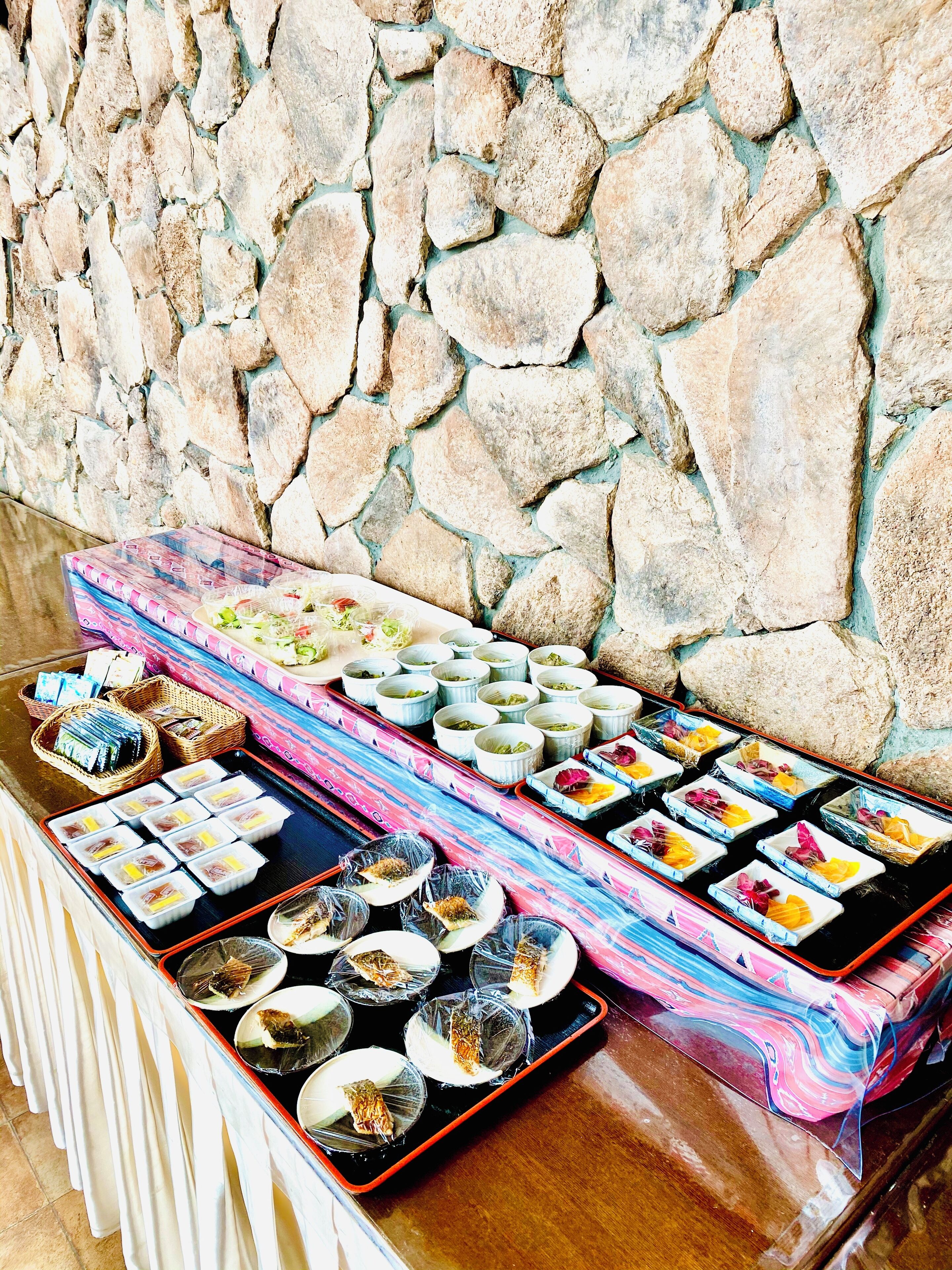 A buffet table with various dishes and drinks, set against a stone wall.