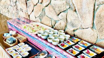 A buffet table with various dishes and drinks, set against a stone wall.