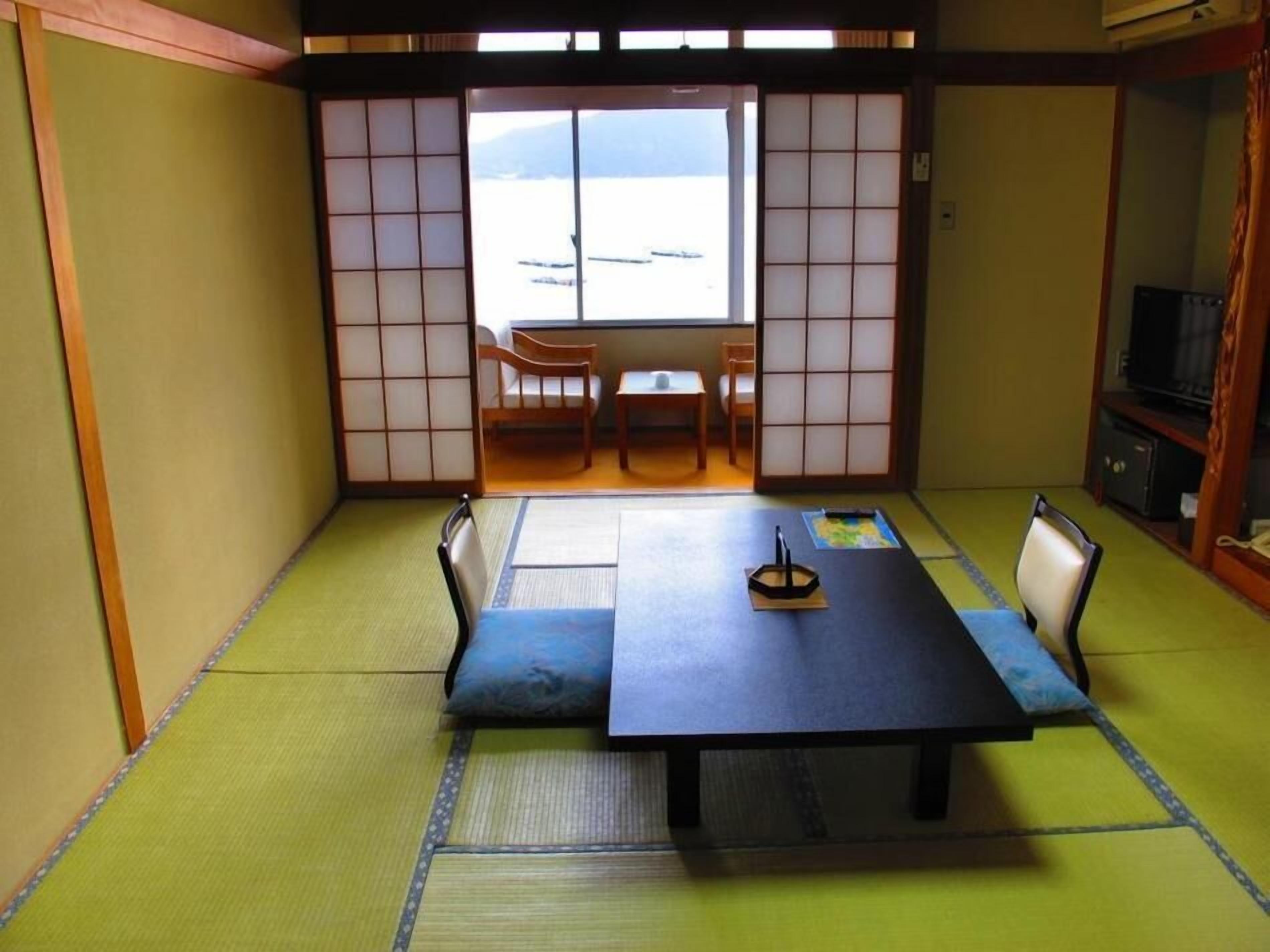 A tatami mat room with a low table and chairs, a sliding door, and a view of the outdoors.