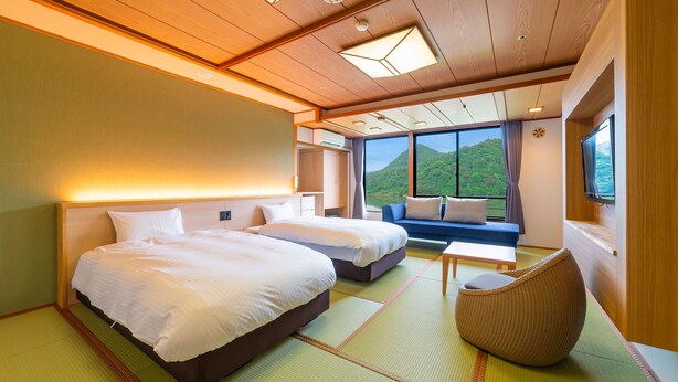 A hotel room with two beds, a sofa, a TV, and a view of a green landscape.