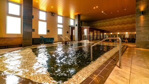 An indoor swimming pool with clear water, metal railings, and a tiled floor.