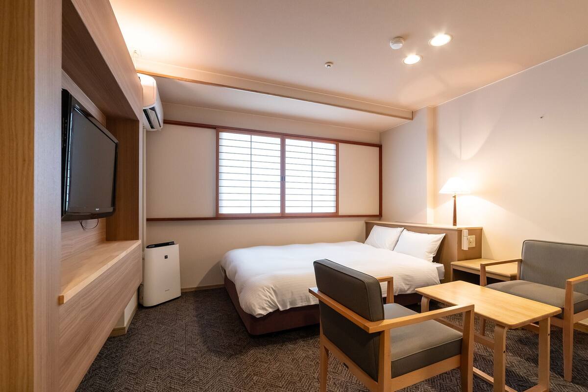 A hotel room with a bed, a desk, a chair, a TV, and a window with blinds.