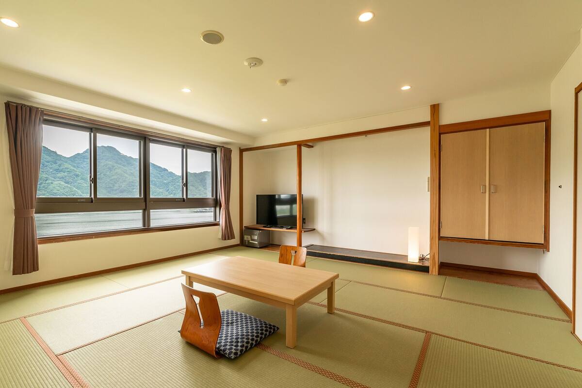 A room with tatami flooring, a television, a cabinet, and a window with a view of mountains.