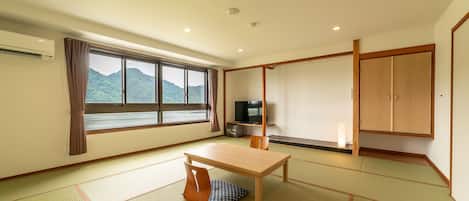 A room with tatami flooring, a television, a cabinet, and a window with a view of mountains.