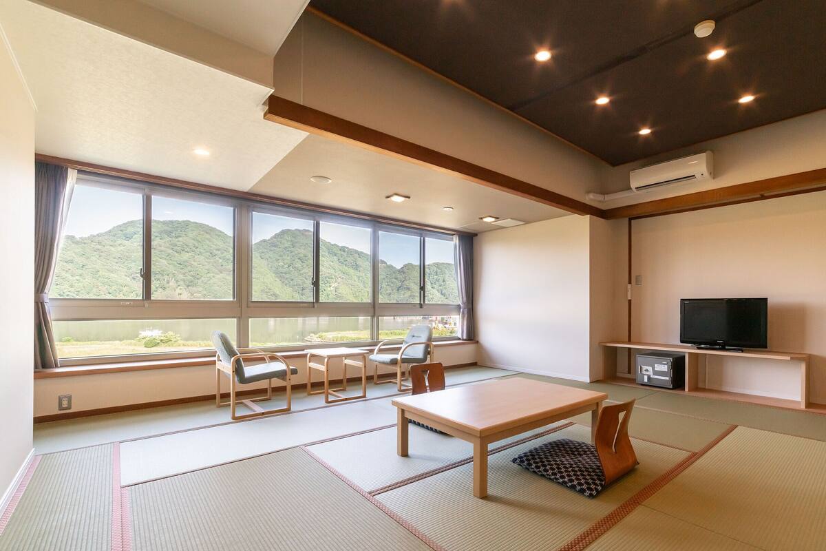 A modern hotel room with tatami mats, a large window with a mountain view, a TV, and a small table.