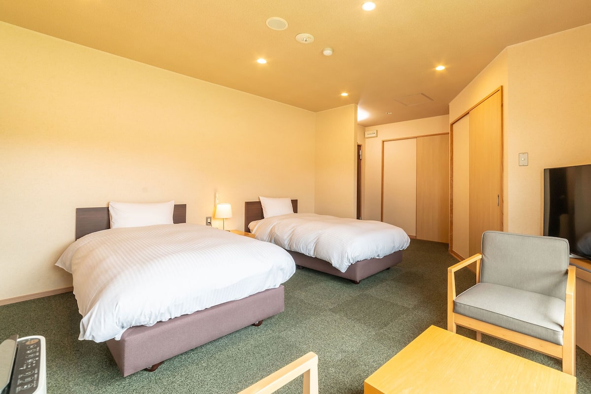 A hotel room with two beds, a TV, a chair, and a desk.