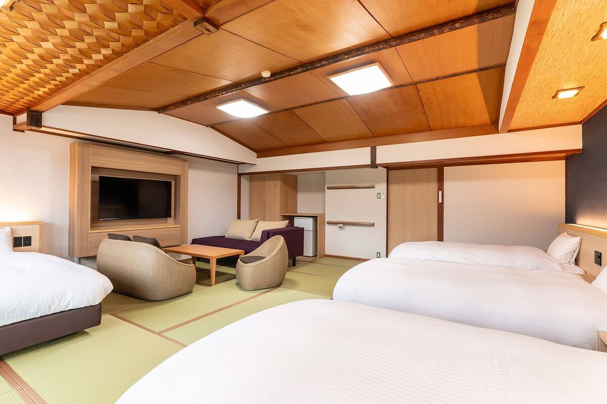 A modern hotel room with two beds, a flat-screen TV, a small table, and a sofa.