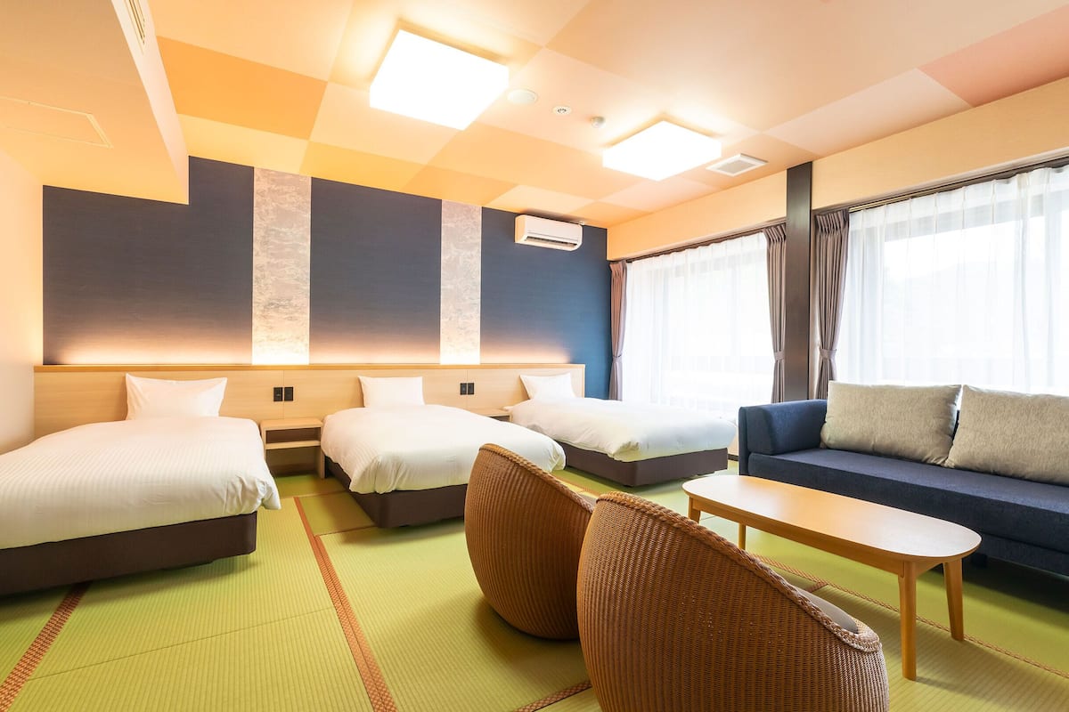 A hotel room with two beds, a sofa, a small table, and a window with curtains.