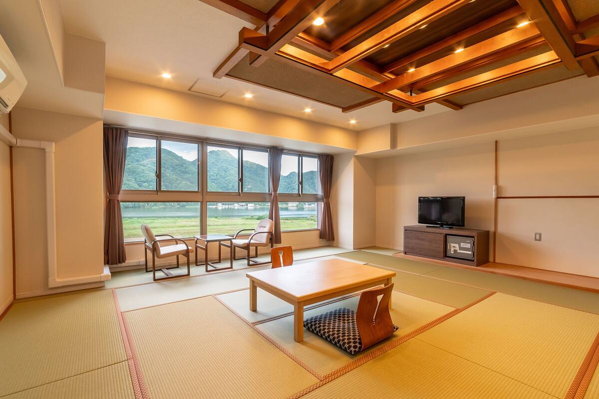 A room with tatami flooring, a television, a table, and chairs.