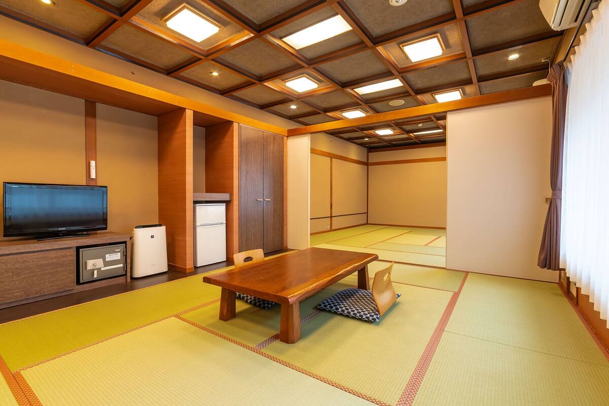 A traditional Japanese-style room with tatami flooring, a low wooden table, a television, and a refrigerator.