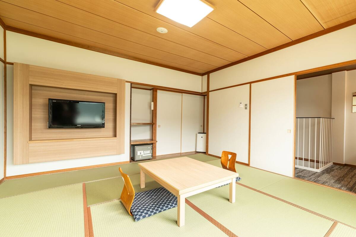 A traditional Japanese room with tatami flooring, a low table, a television, and sliding doors.