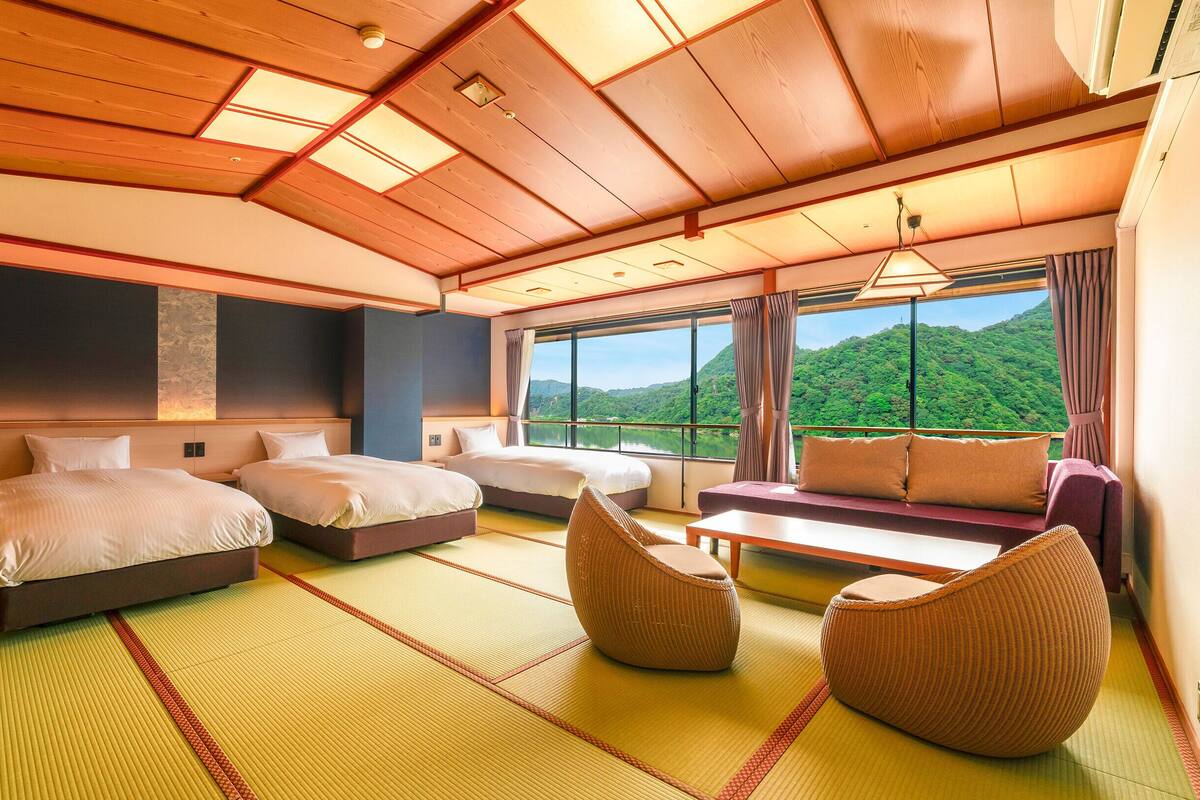 A hotel room with two beds, a sofa, and a view of a green landscape.
