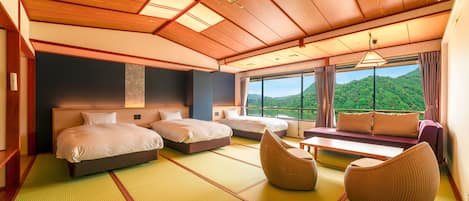 A hotel room with two beds, a sofa, and a view of a green landscape.