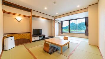 A hotel room with tatami flooring, a television, a small table, and a window with a mountain view.