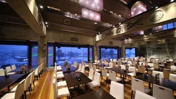 A spacious restaurant with high ceilings, modern chandeliers, and large windows offering views of the snowy outdoors.