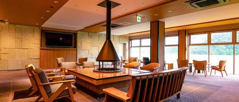 Un área de estar moderna con chimenea, asientos cómodos, un televisor de pantalla plana y ventanas amplias con vistas al exterior.