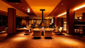 A warmly lit lounge area with a central table, chairs, and a decorative lamp.