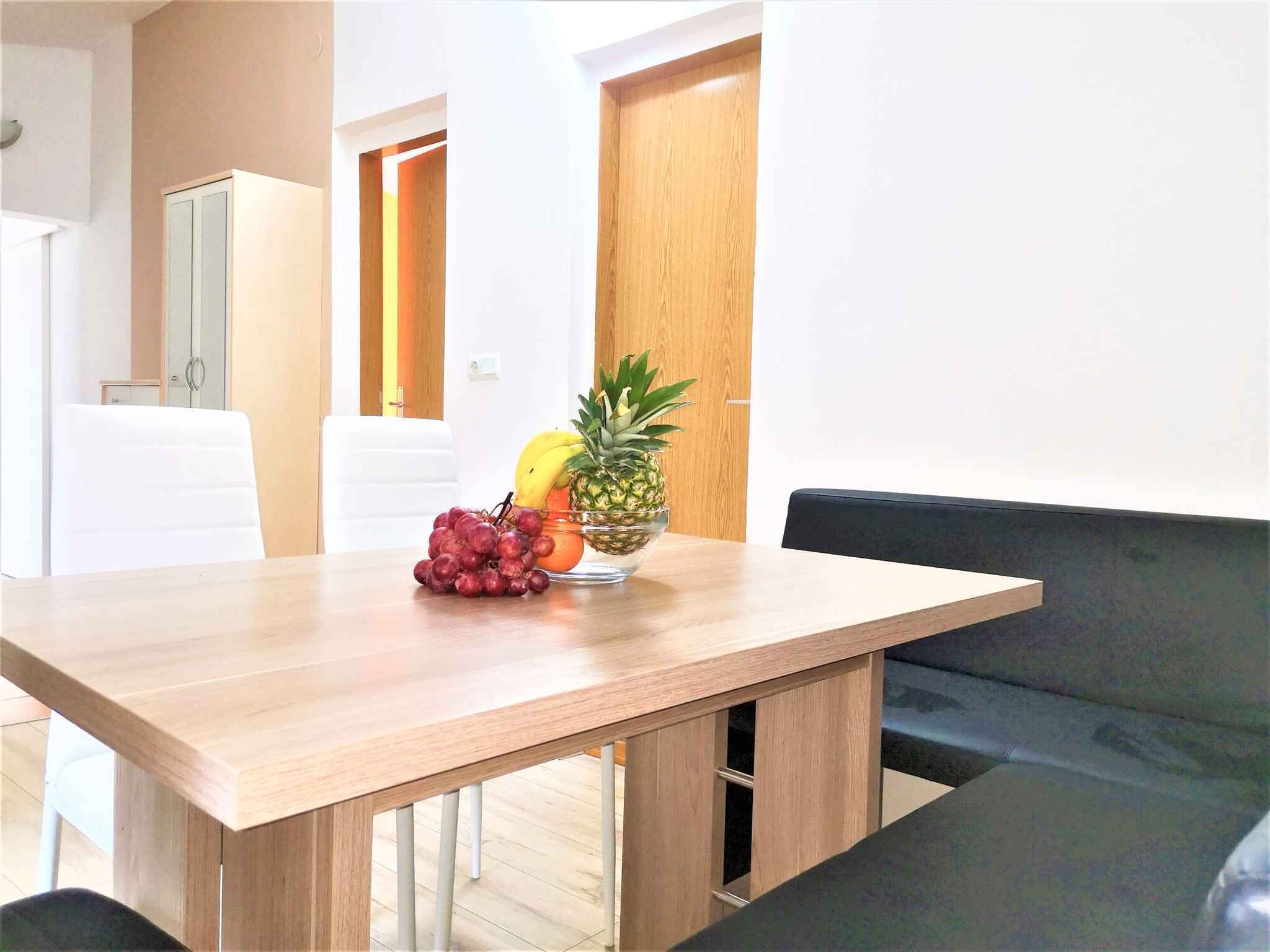 Ein moderner Essbereich mit einem Holztisch, einer schwarzen gepolsterten Bank und einer Obstschale mit Trauben, einer Ananas und einer Banane.