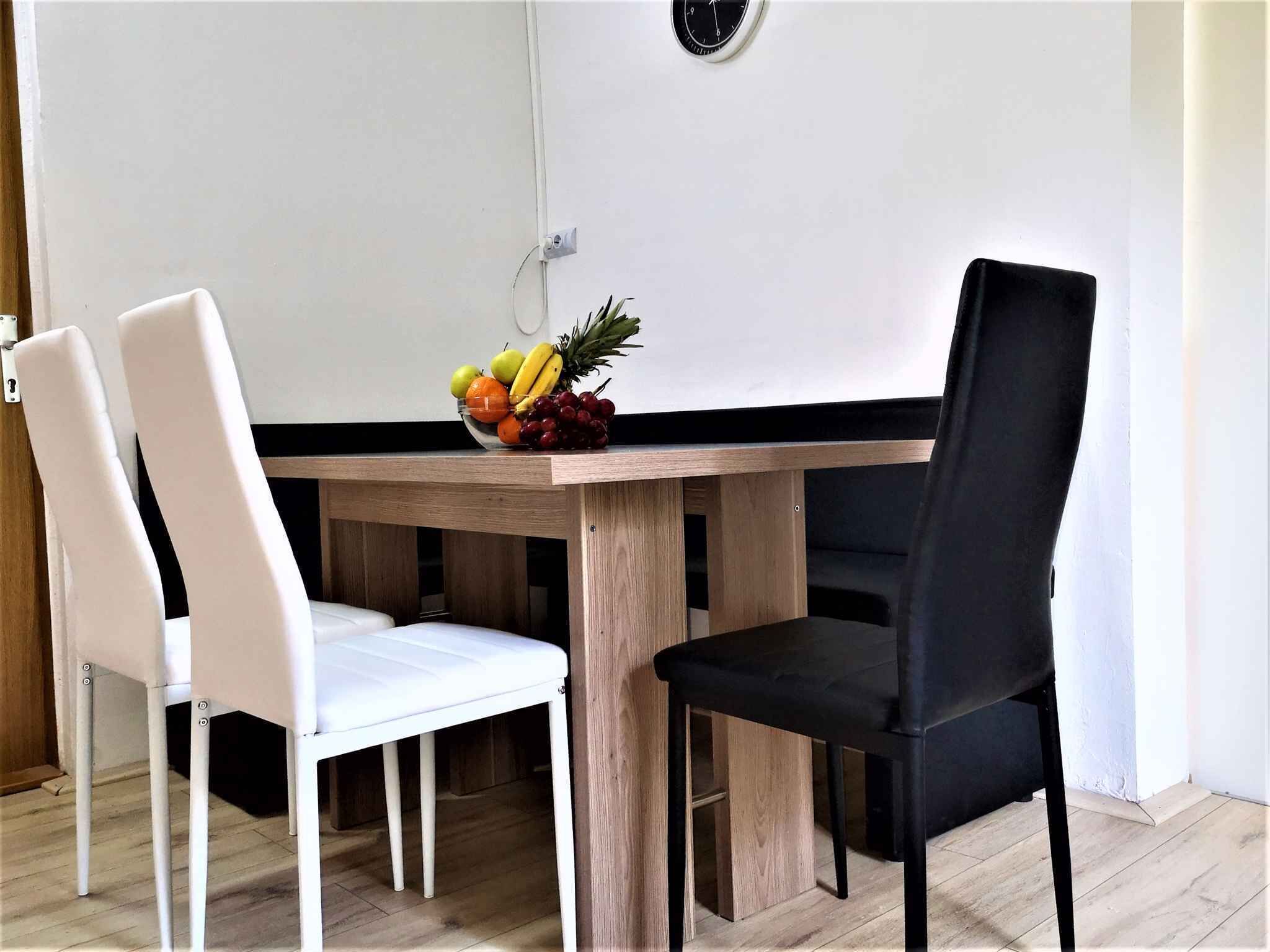 Un tavolo da pranzo con due sedie, una bianca e una nera, e una ciotola di frutta sopra.