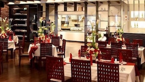 Un restaurante con mesas dispuestas para comer, con sillas rojas y manteles blancos.