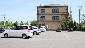 Un estacionamiento con varios autos y un edificio de ladrillo con ventanas arqueadas.