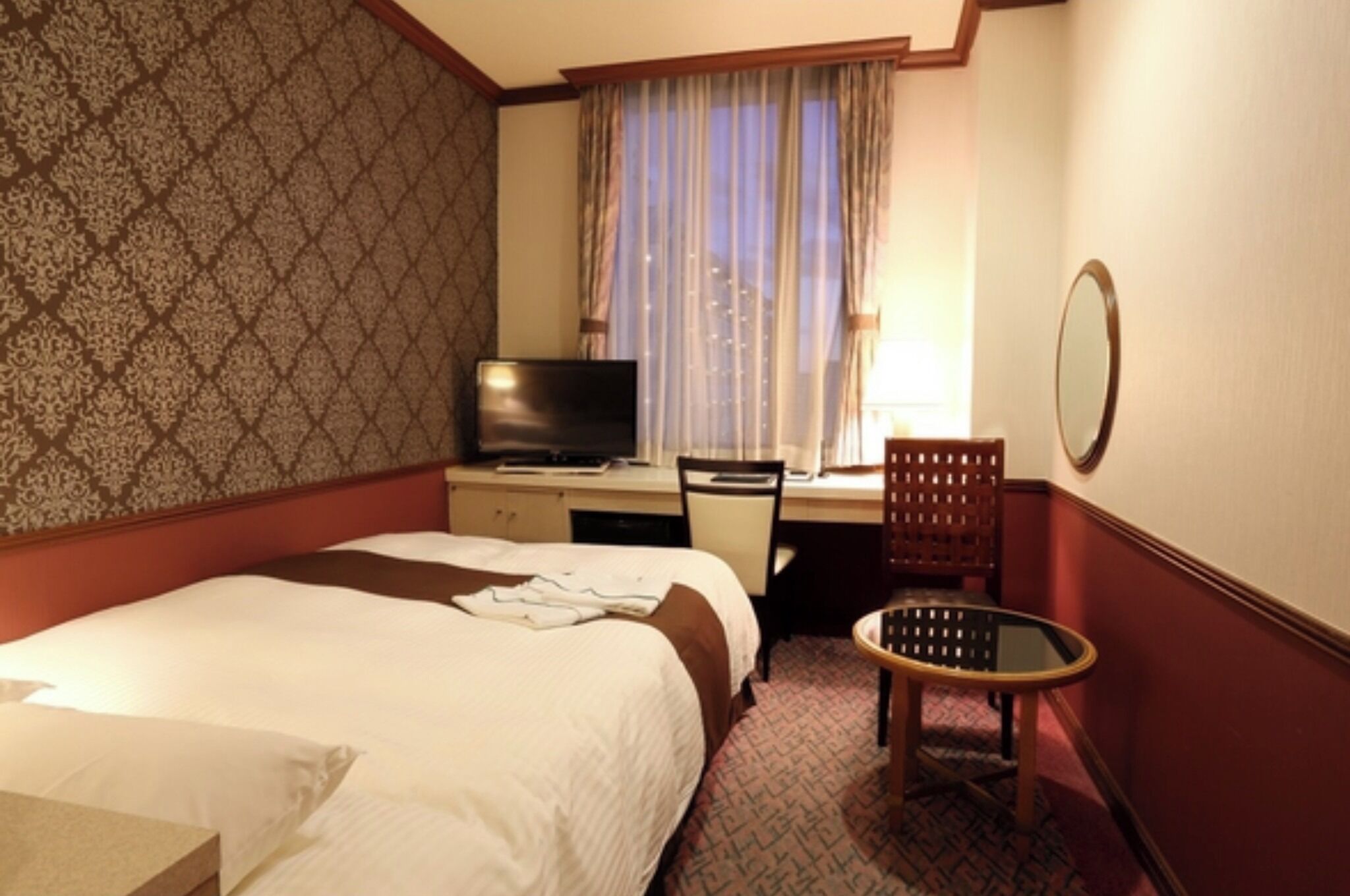 Ein Hotelzimmer mit Bett, Schreibtisch mit Fernseher, Stuhl und kleinem Tisch.